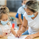 Early Childcare worker wearing mask, teaching child in mask