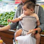 Mother holding baby shopping for food.