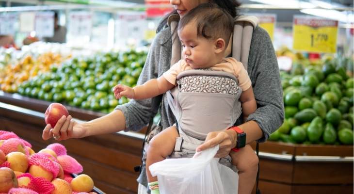 Mother holding baby shopping for food.