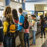 Children standing in line for school lunch, wearing backpacks